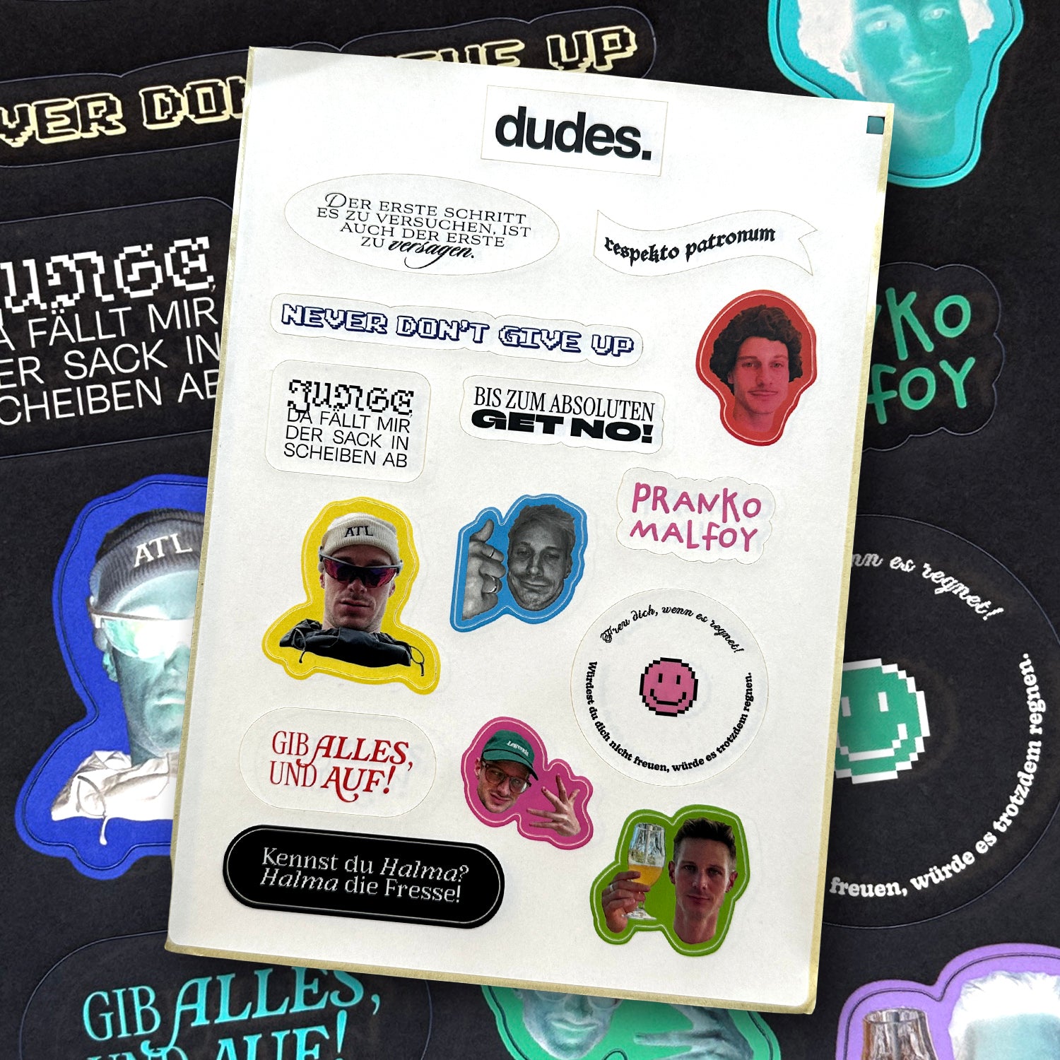 Nahaufnahme eines Stickerbogens auf schwarzem Hintergrund mit bunten Motiven: Aufkleber mit Sprüchen wie „NEVER DON'T GIVE UP“, „respekto patronum“, „GIB ALLES, UND AUF!“, „Kennst du Halma? Halma die Fresse!“ sowie „PRANKO MALFOY“. Dazu Porträtfotos von Personen mit Sonnenbrille, Cap oder Glas in der Hand, teils als Umrisssticker. Zentral oben: dudes.-Logo.